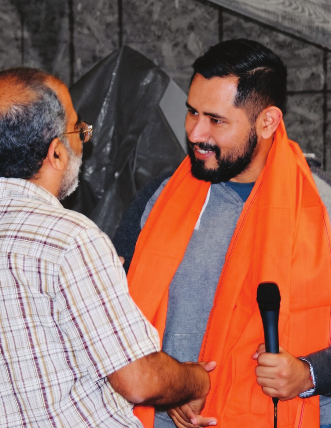 Marcelo Olvera speaking with a microphone, greeting a colleague